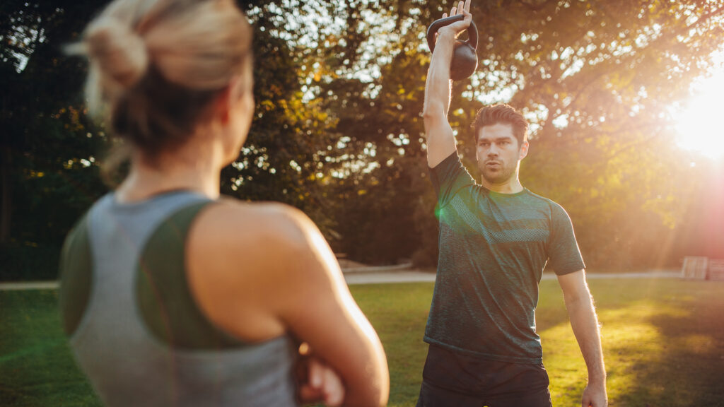 Healthy young man with female trainer exercising with kettlebell in the park.